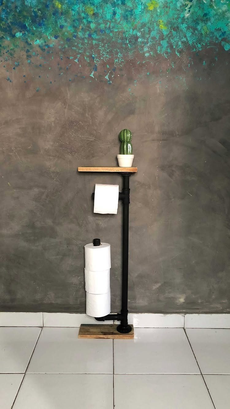 A black metal pipe toilet paper holder with a wooden shelf and two rolls of paper.