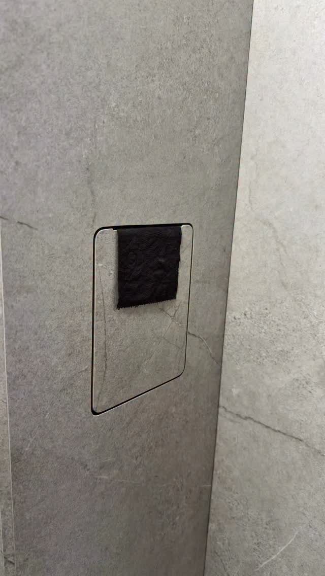 A black rectangular recessed niche in a grey tiled wall holding a roll of dark toilet paper.