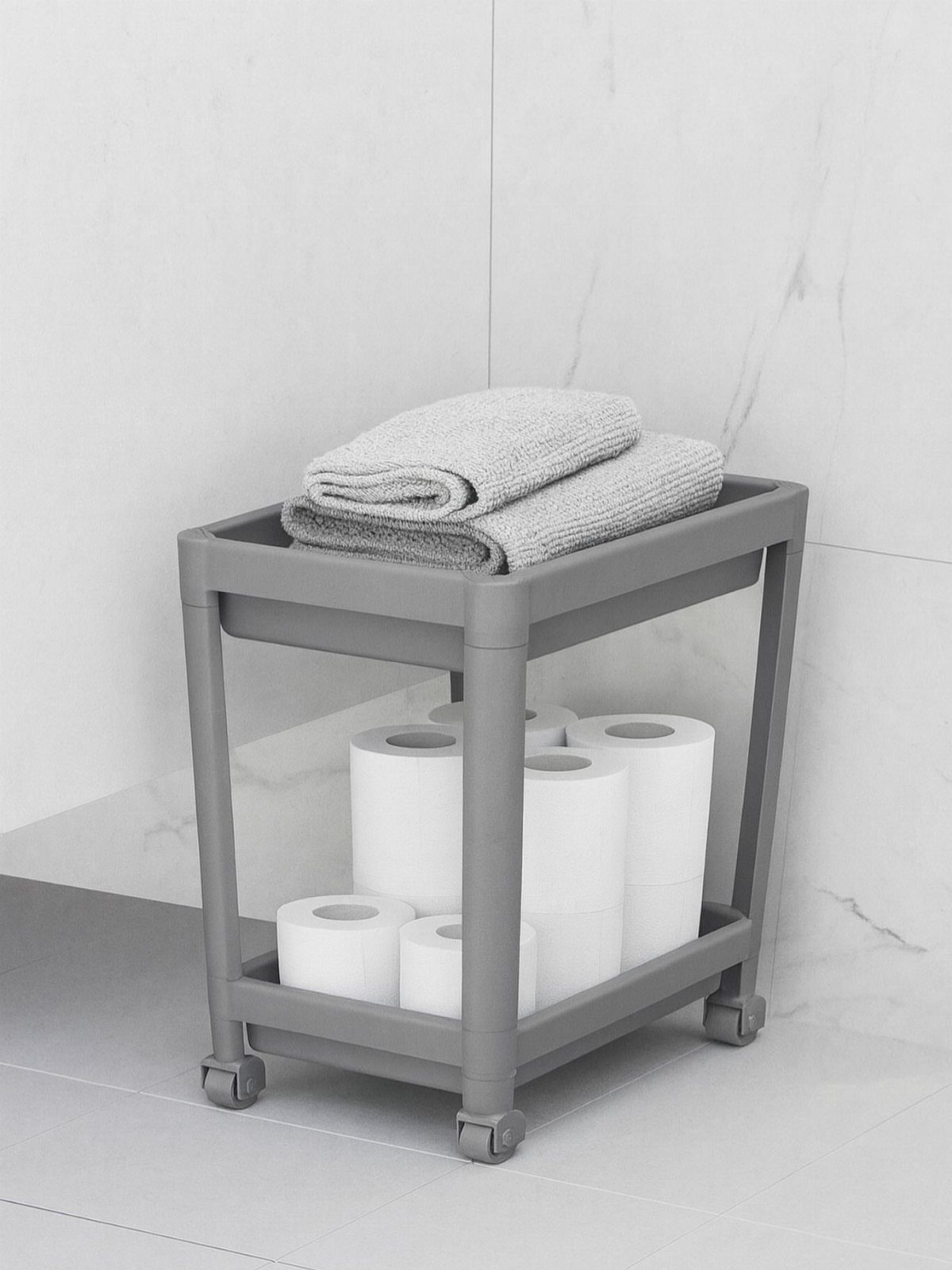 A grey two-tier plastic rolling cart holding folded towels and rolls of white toilet paper.