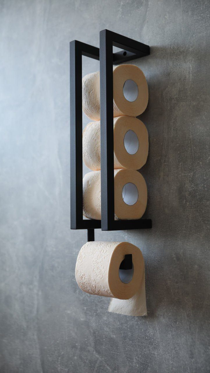 Black metal wall-mounted toilet paper holder rack holding four rolls against a grey wall.