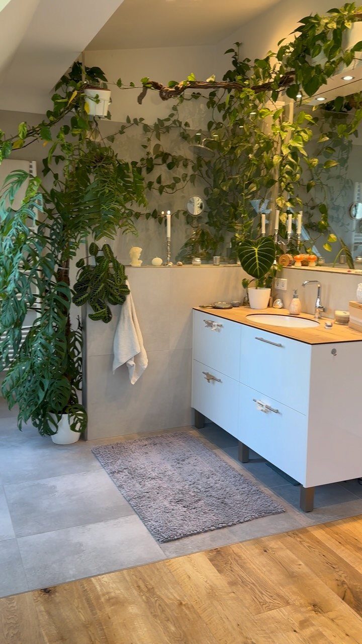 Lush green plants and climbing vines decorating a bright modern bathroom with a white vanity.