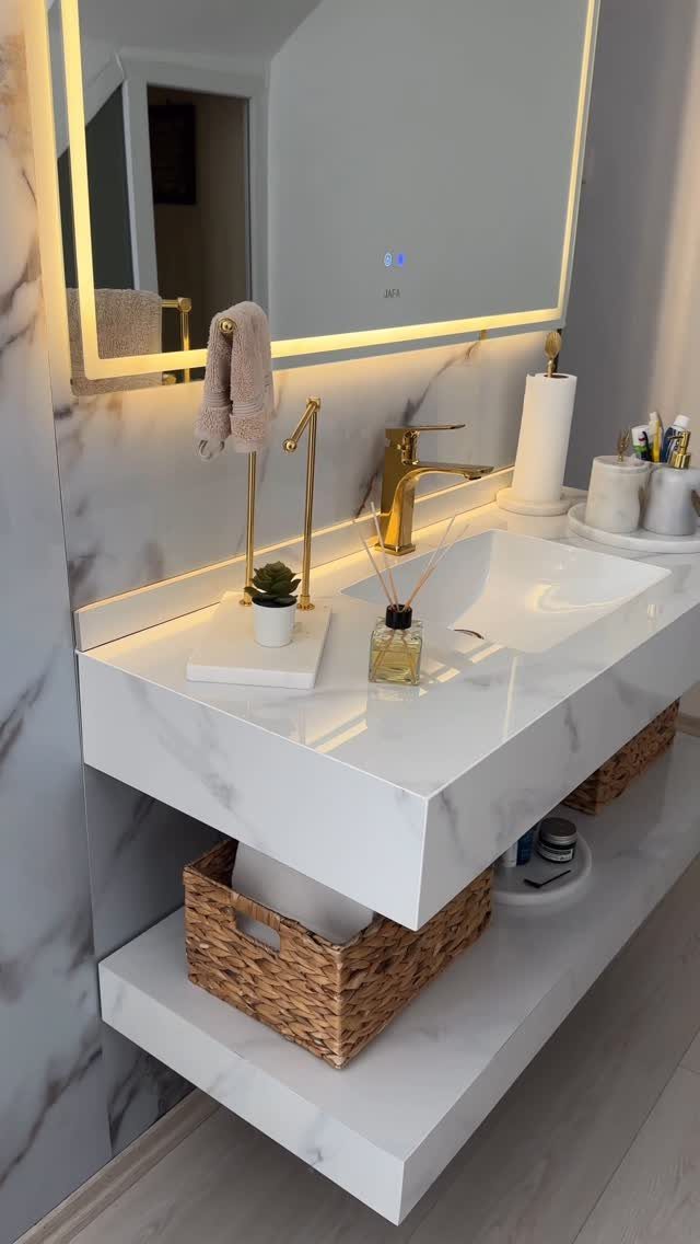 White marble bathroom vanity with gold fixtures and organized accessories on trays.