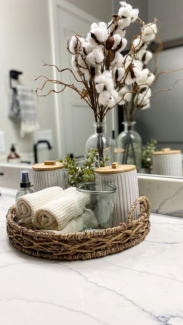 Woven basket tray containing rolled towels and canisters on a marble bathroom countertop.
