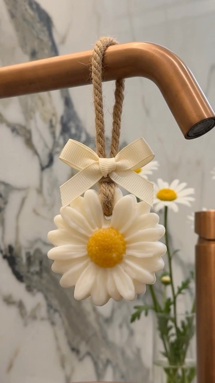 A white daisy-shaped soap with a cream bow hanging from a copper bathroom faucet.