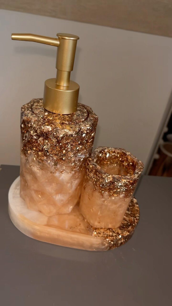 Gold and peach resin soap dispenser and matching cup set on a tray.