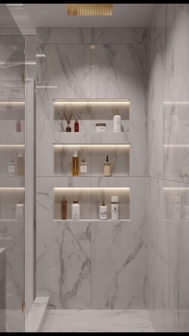 Recessed illuminated wall niches containing various toiletries set against white marble bathroom tiles.