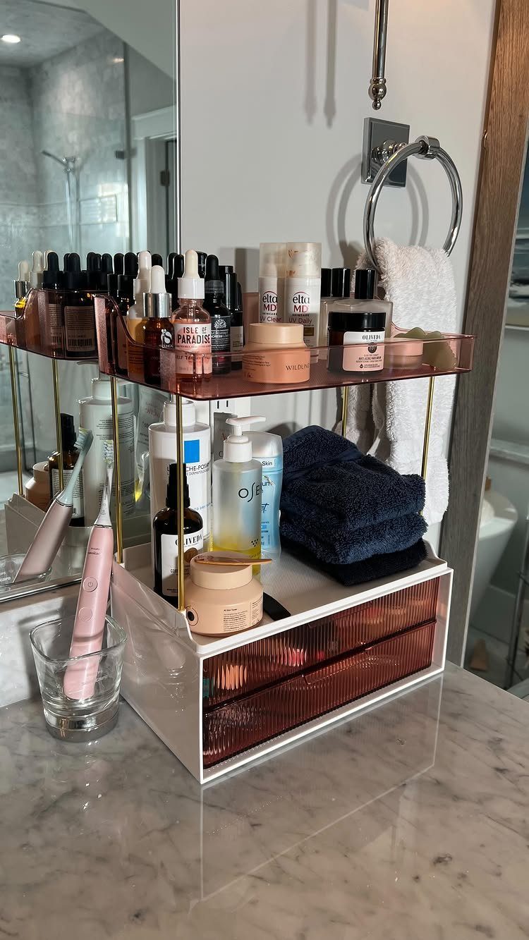Acrylic skincare organizer with gold accents holding various beauty products and towels on a marble counter.
