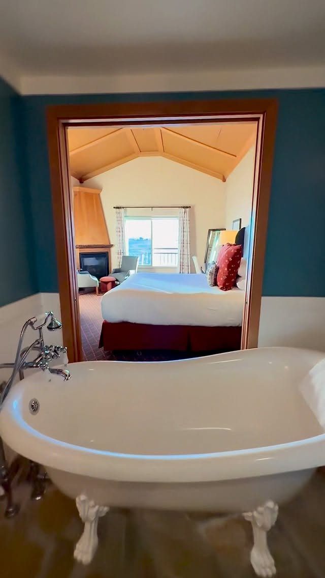 A white claw-foot bathtub positioned in front of an open doorway leading to a bedroom.