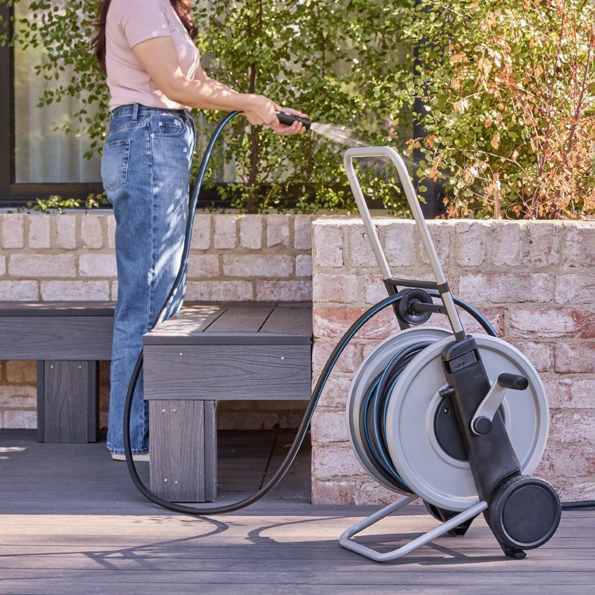 A person using a garden hose while it is neatly stored on a metal hose reel stand.