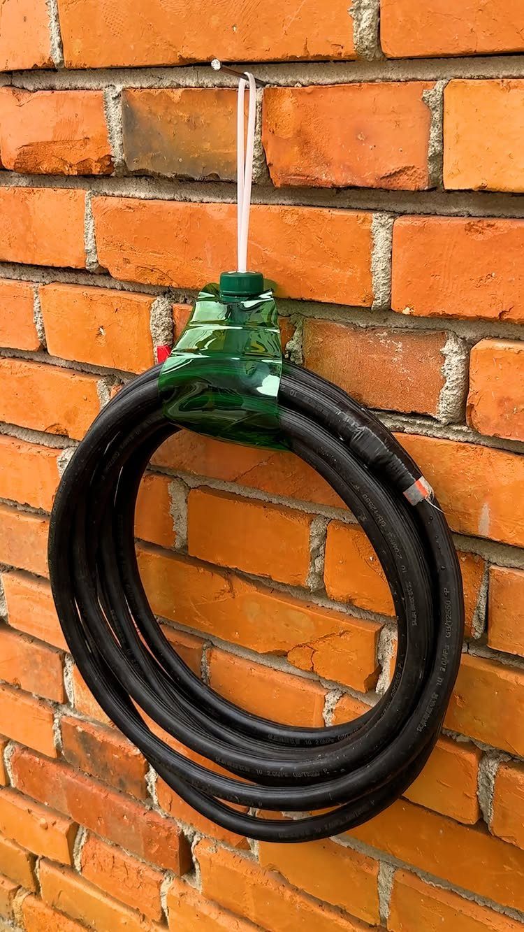 A coiled black garden hose hanging from a green plastic bottle on a brick wall.