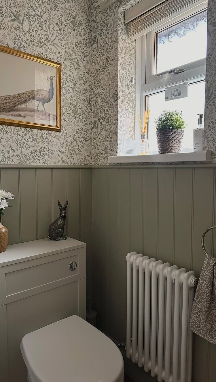 Sage green wainscoting and botanical patterned wallpaper in a bathroom corner with a white toilet.