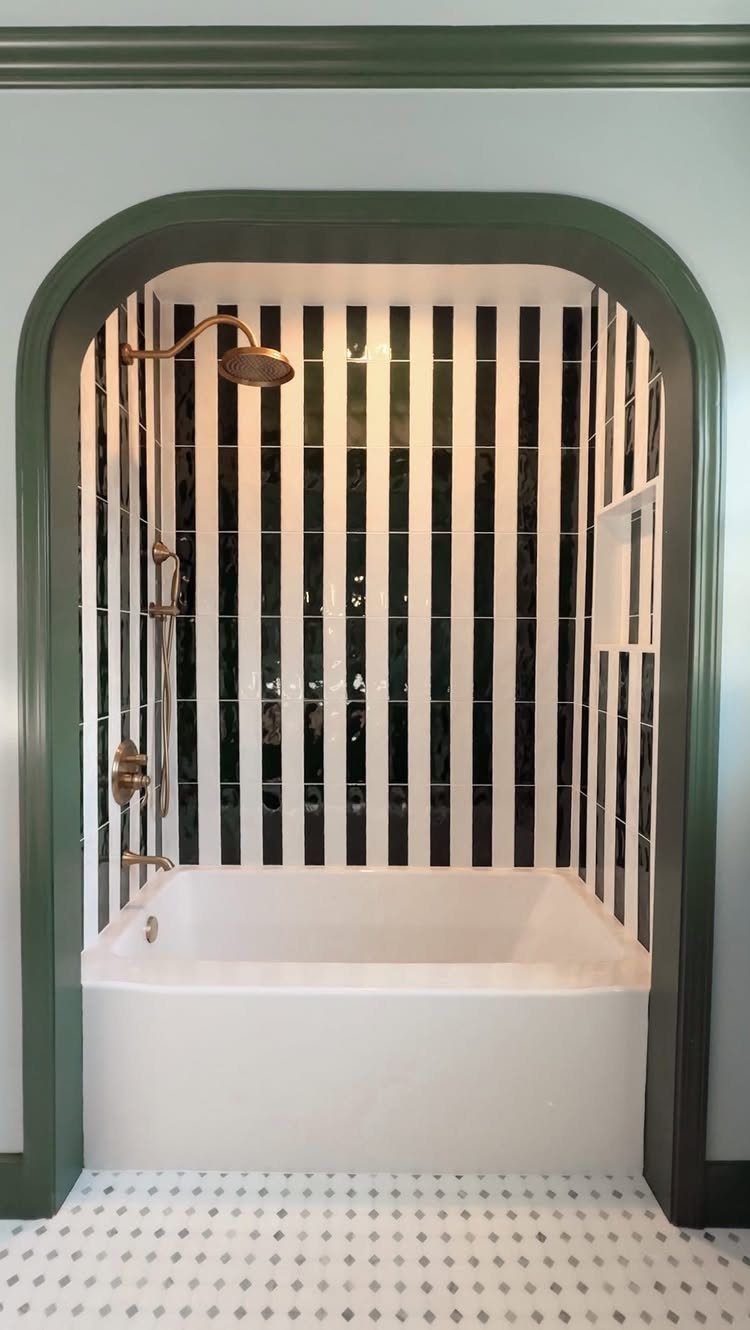 A white bathtub installed in an arched alcove with black and white striped tiles.