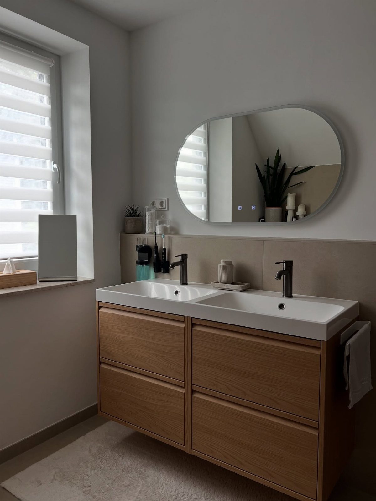 A wooden double-sink vanity with black faucets and an oval mirror in a bright bathroom.