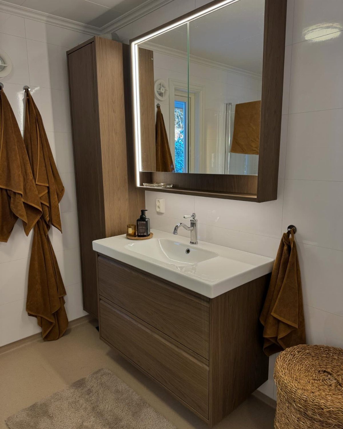 A modern bathroom vanity with dark wood cabinetry, a white sink, and a large backlit mirror.