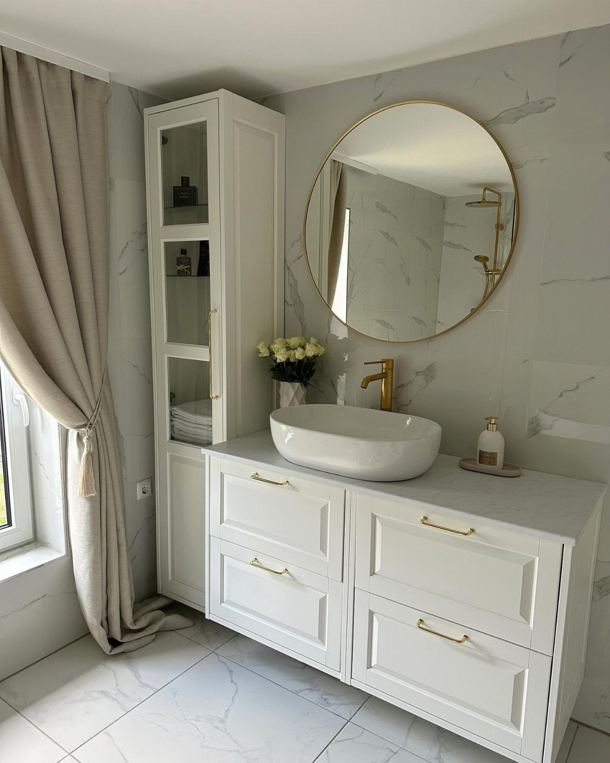 White double-drawer vanity with gold hardware, a vessel sink, and a large round gold-rimmed mirror.