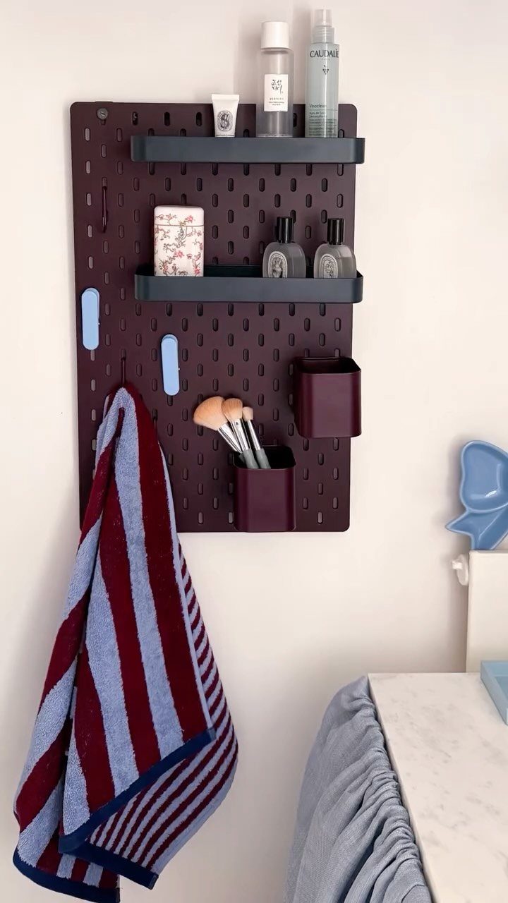 A dark purple pegboard wall unit holding cosmetic bottles, makeup brushes, and a striped towel.