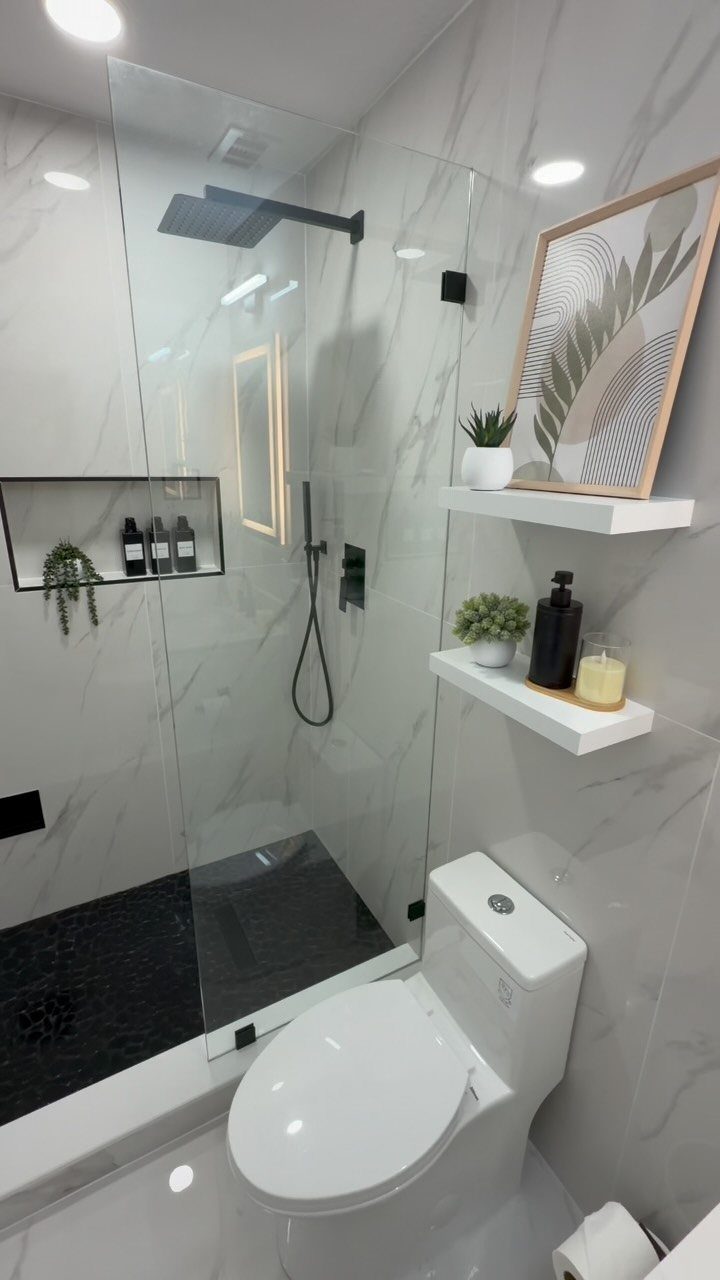 White marble bathroom with a glass shower, white toilet, and floating shelves on the wall.