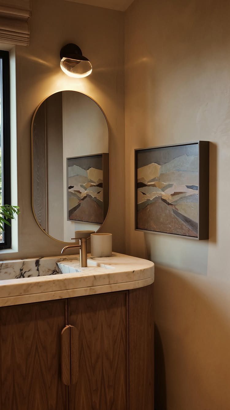 A wooden bathroom vanity with a marble countertop and an oval mirror on a beige wall.