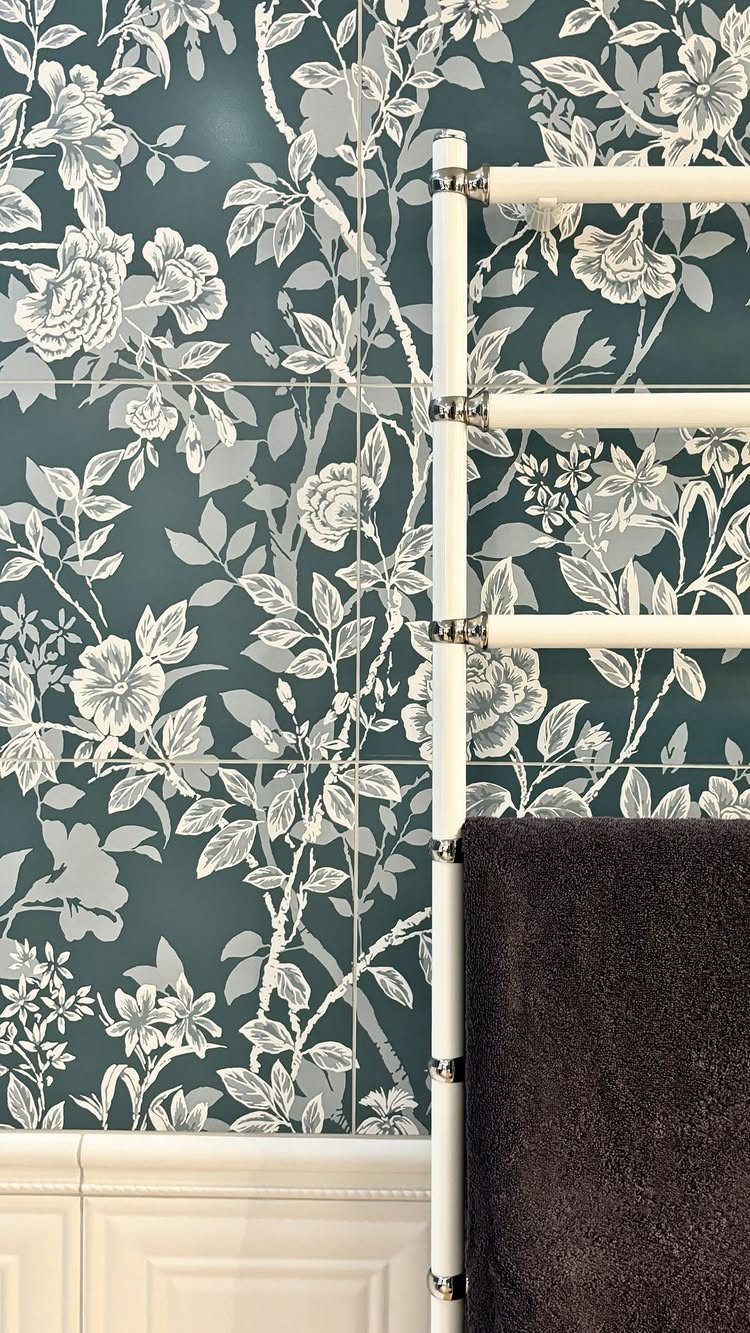 Floral patterned teal and white tiles covering a bathroom wall next to a white towel rail.
