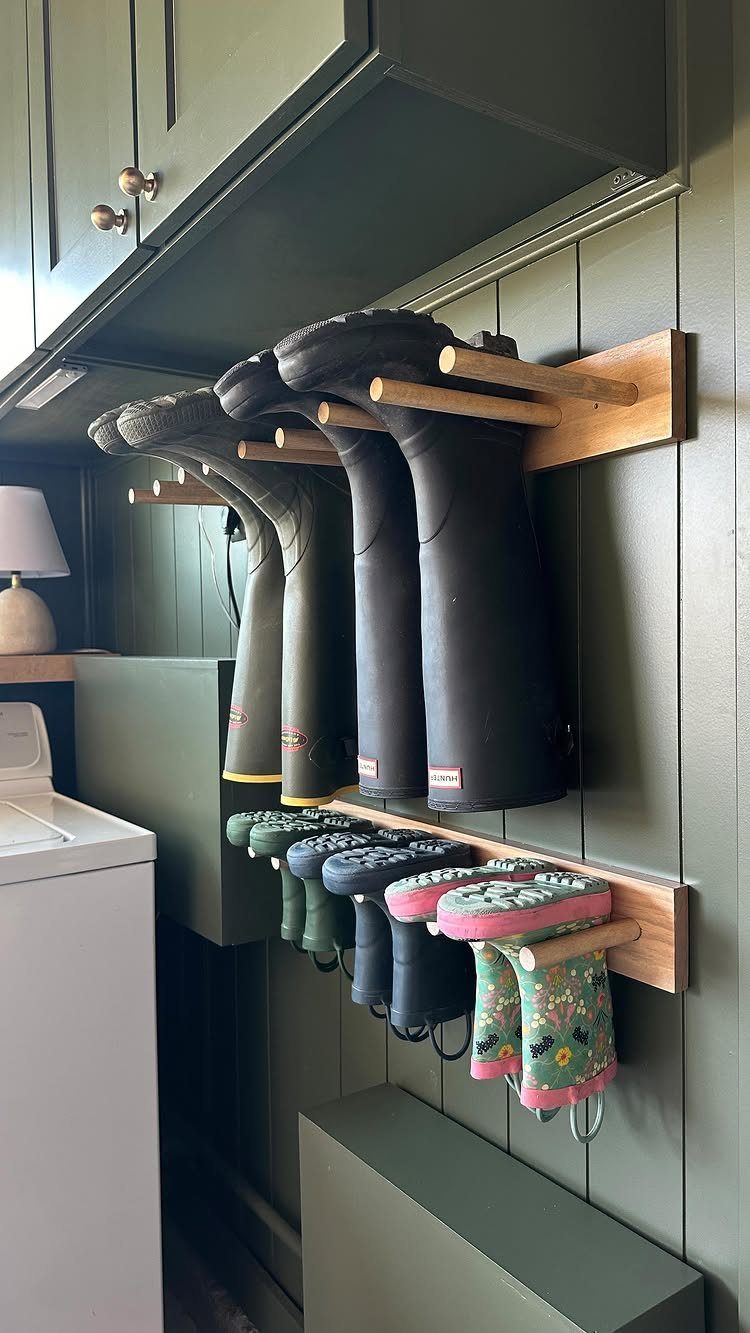 Rubber rain boots hanging from wooden racks mounted on a green paneled wall.