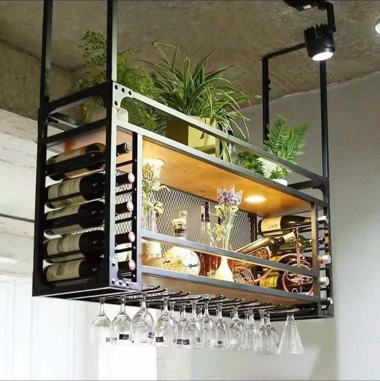 Industrial black metal rack hanging from a ceiling holding plants, wine bottles, and glassware.
