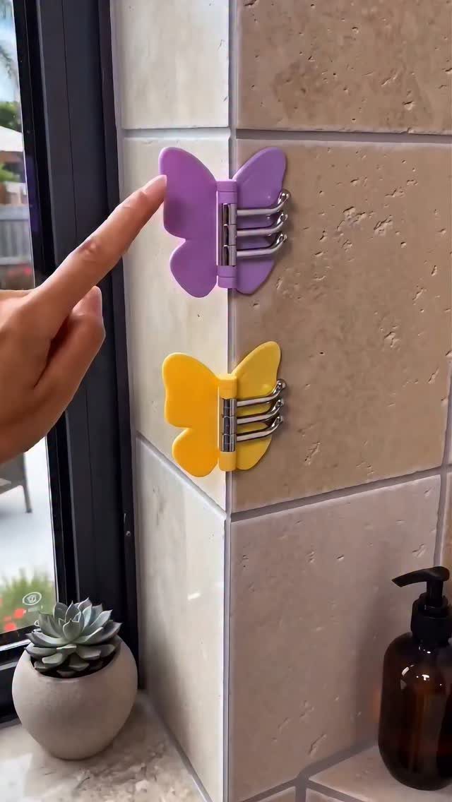 A hand pointing to purple and yellow butterfly-shaped hooks mounted on a tiled wall.