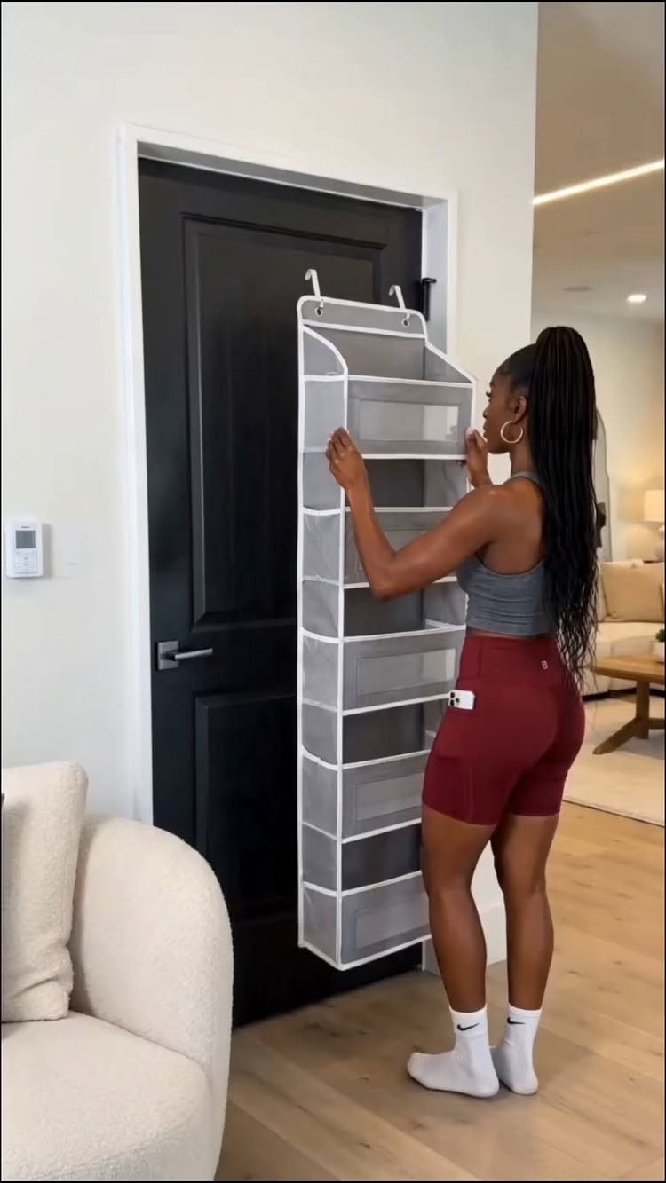 A woman organizing items in a white mesh over-the-door storage organizer hanging on a black door.