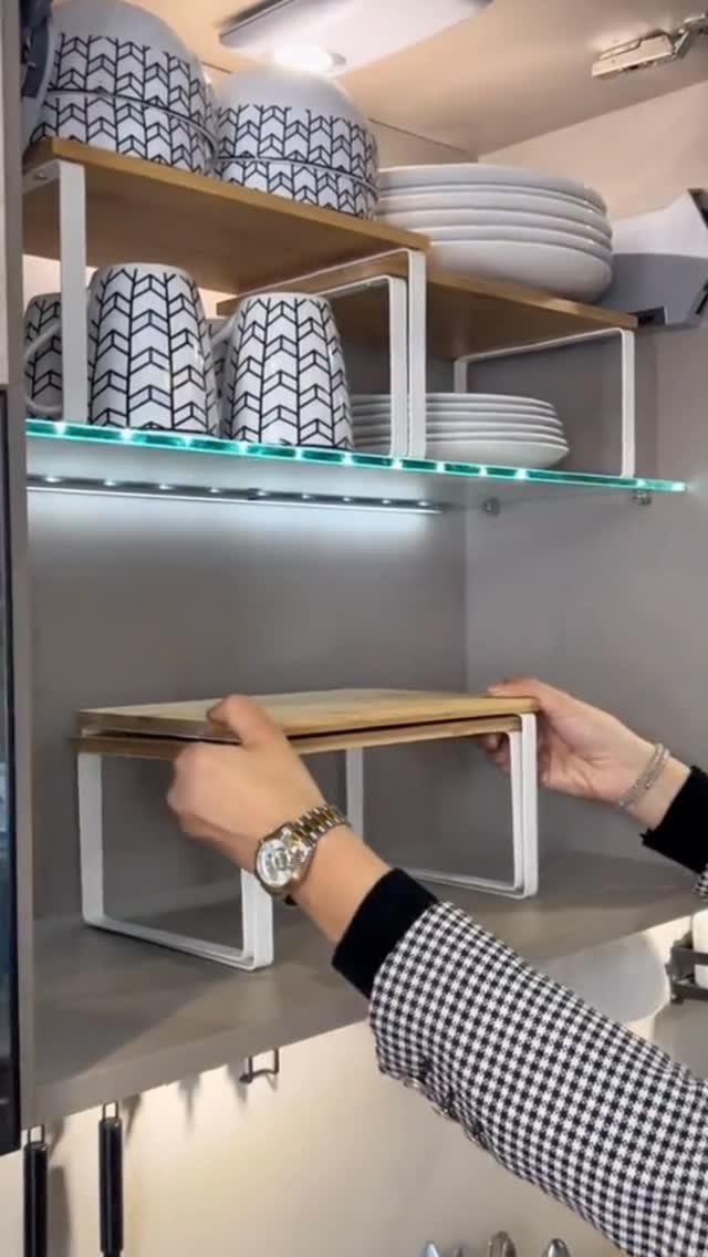 Hands placing a wooden and metal shelf riser onto a kitchen cabinet shelf.