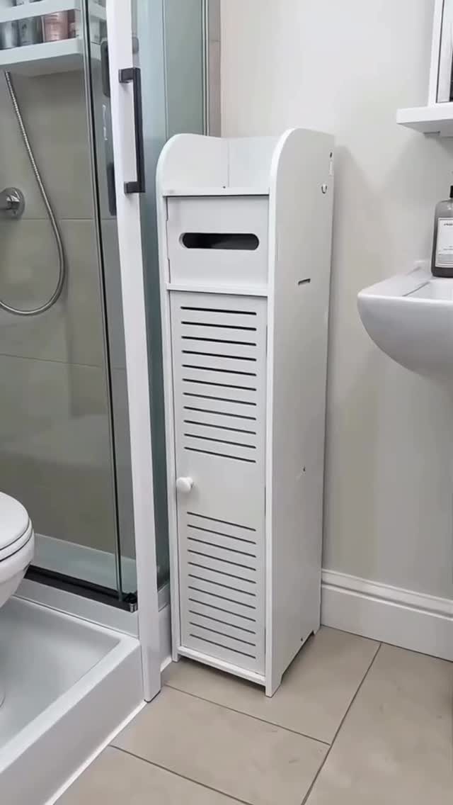 A tall, narrow white wooden storage cabinet positioned in a bathroom between a shower and sink.