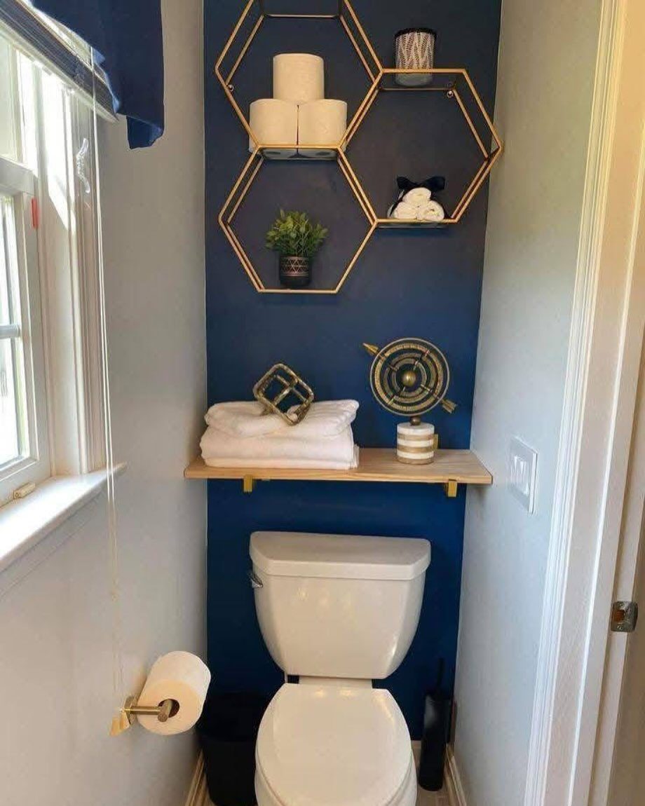 A navy blue accent wall in a bathroom with gold hexagonal shelves and a white toilet.