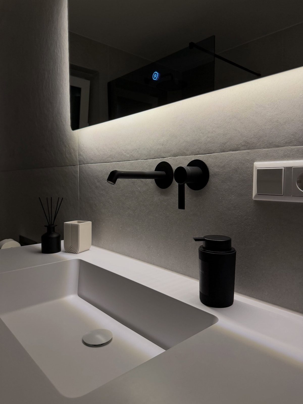 A white rectangular sink with a matte black wall-mounted faucet and grey textured walls.