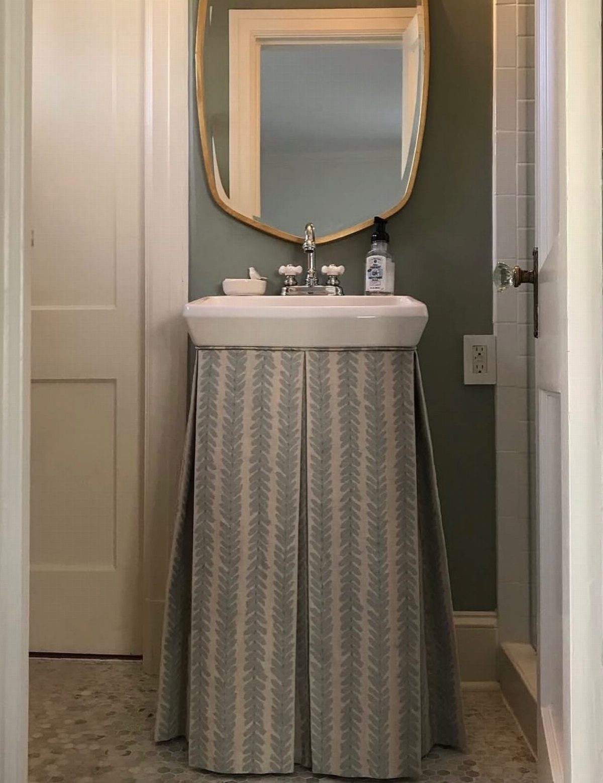 A white ceramic sink featuring a decorative grey patterned fabric skirt against a green wall.