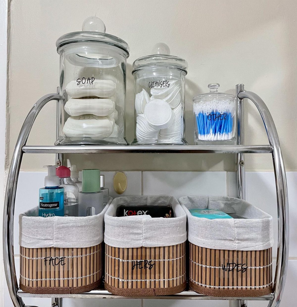 Glass storage jars containing soap, cotton pads, and cotton swabs on a metal bathroom shelf.