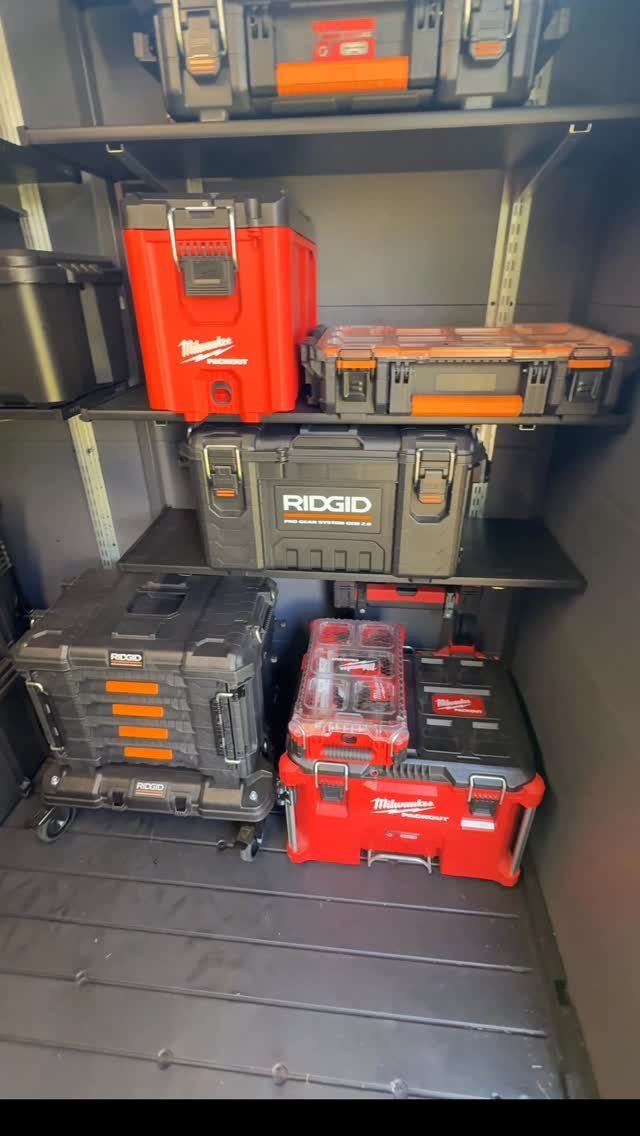 Black adjustable metal shelves holding several red and black heavy-duty toolboxes in a storage area.