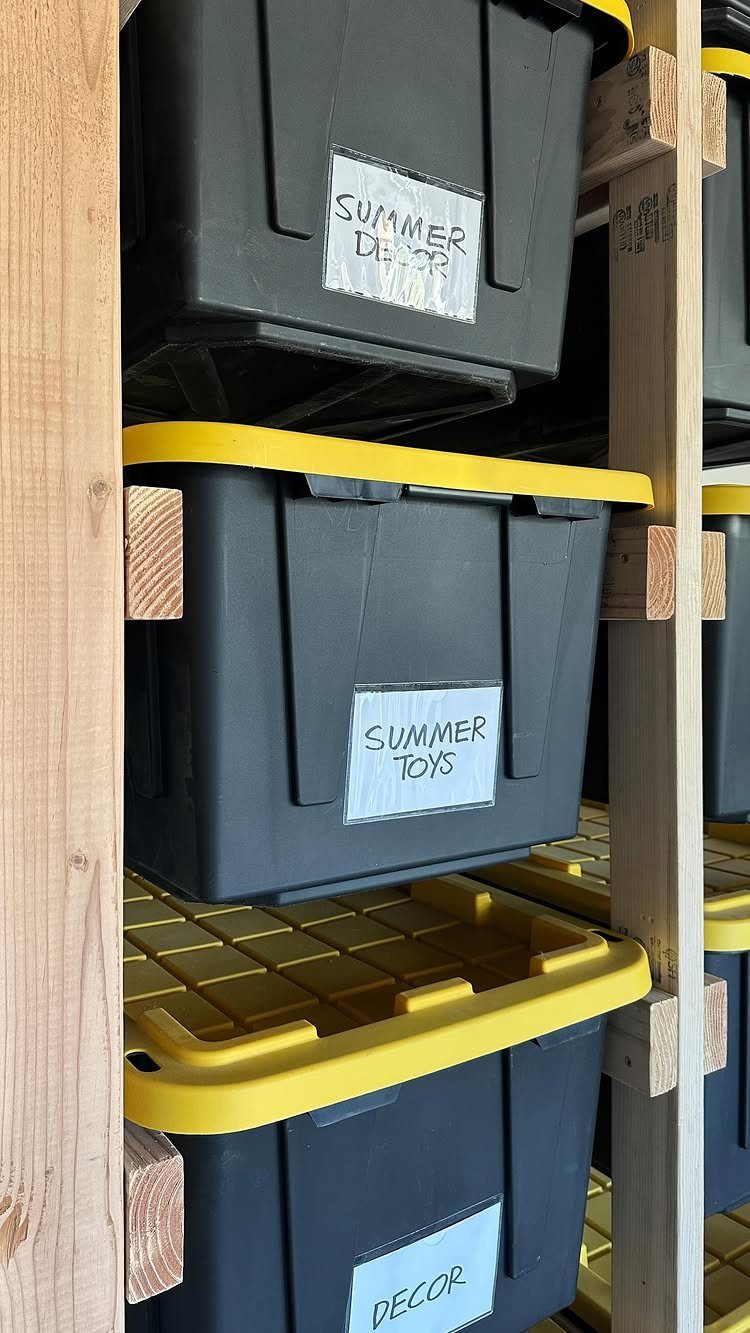 Black storage bins with yellow lids and handwritten labels sit on wooden shelving units.