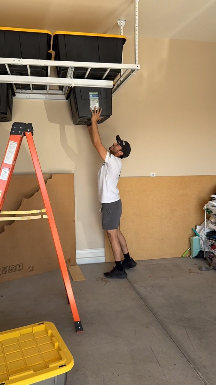 A man reaching up to adjust a black storage bin on a white overhead rack system.