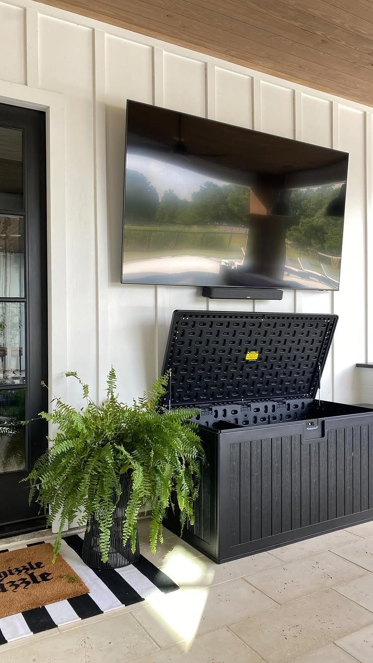 A black outdoor deck box with an open lid sits on a patio next to a fern.