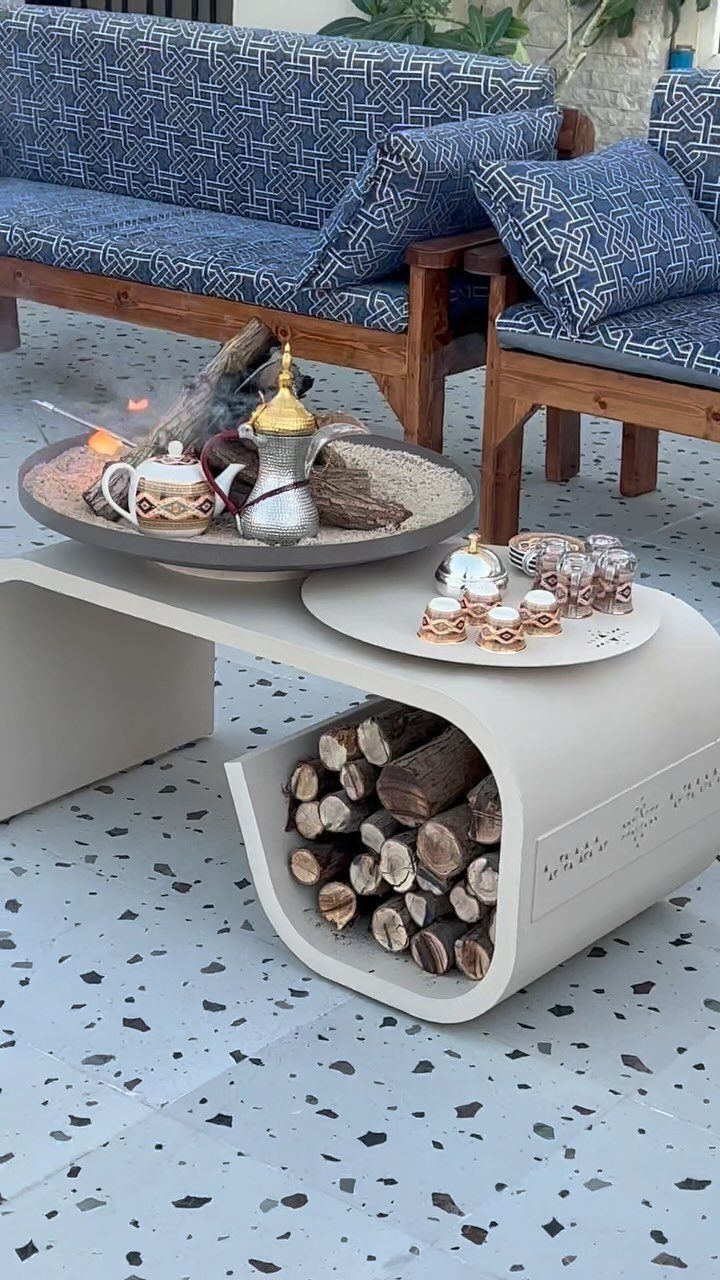 A modern light-colored outdoor coffee table with a built-in compartment filled with firewood logs.