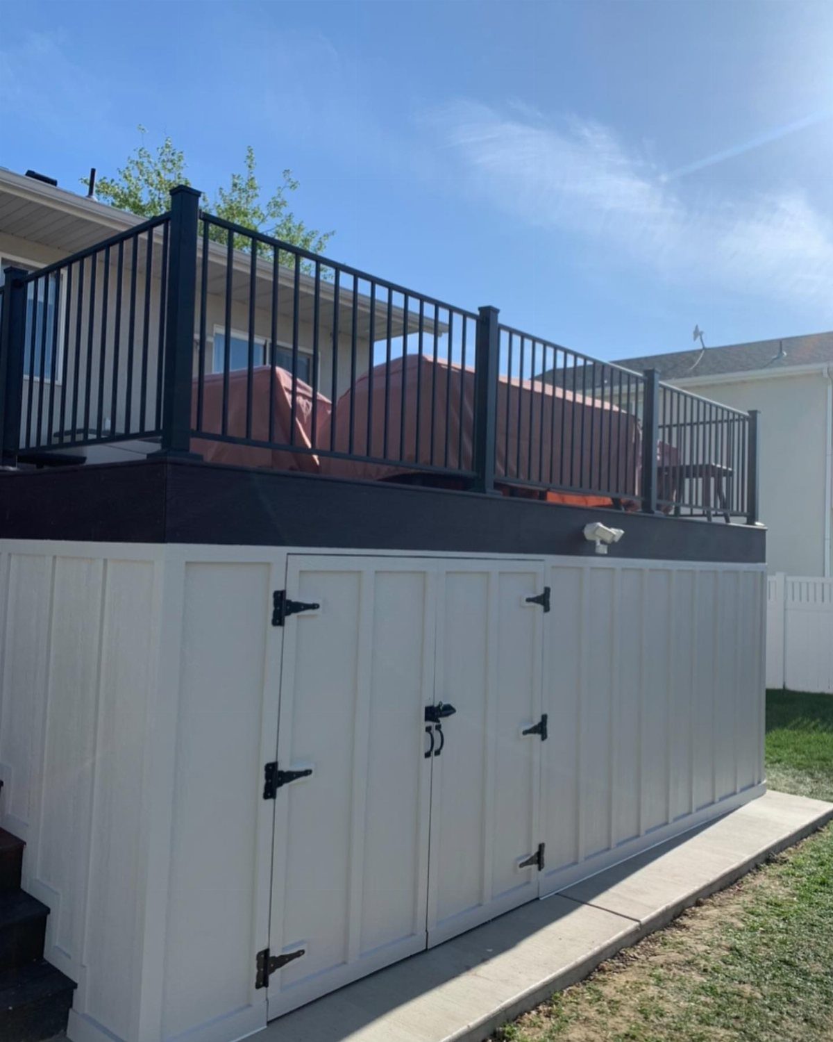 White paneled storage enclosure built underneath a raised wooden deck with black railings.