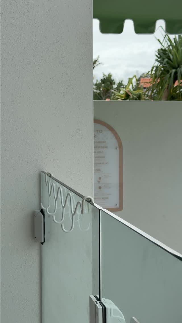 White wavy hooks mounted on a glass railing attached to a white wall.