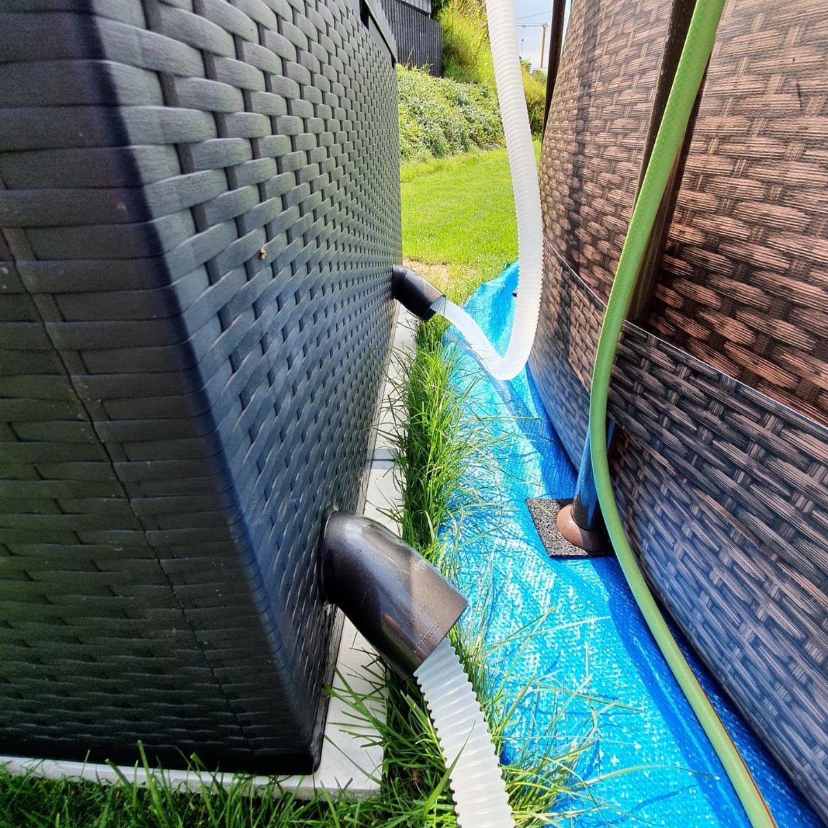 Black wicker storage box with white hoses connected near a blue above-ground pool.