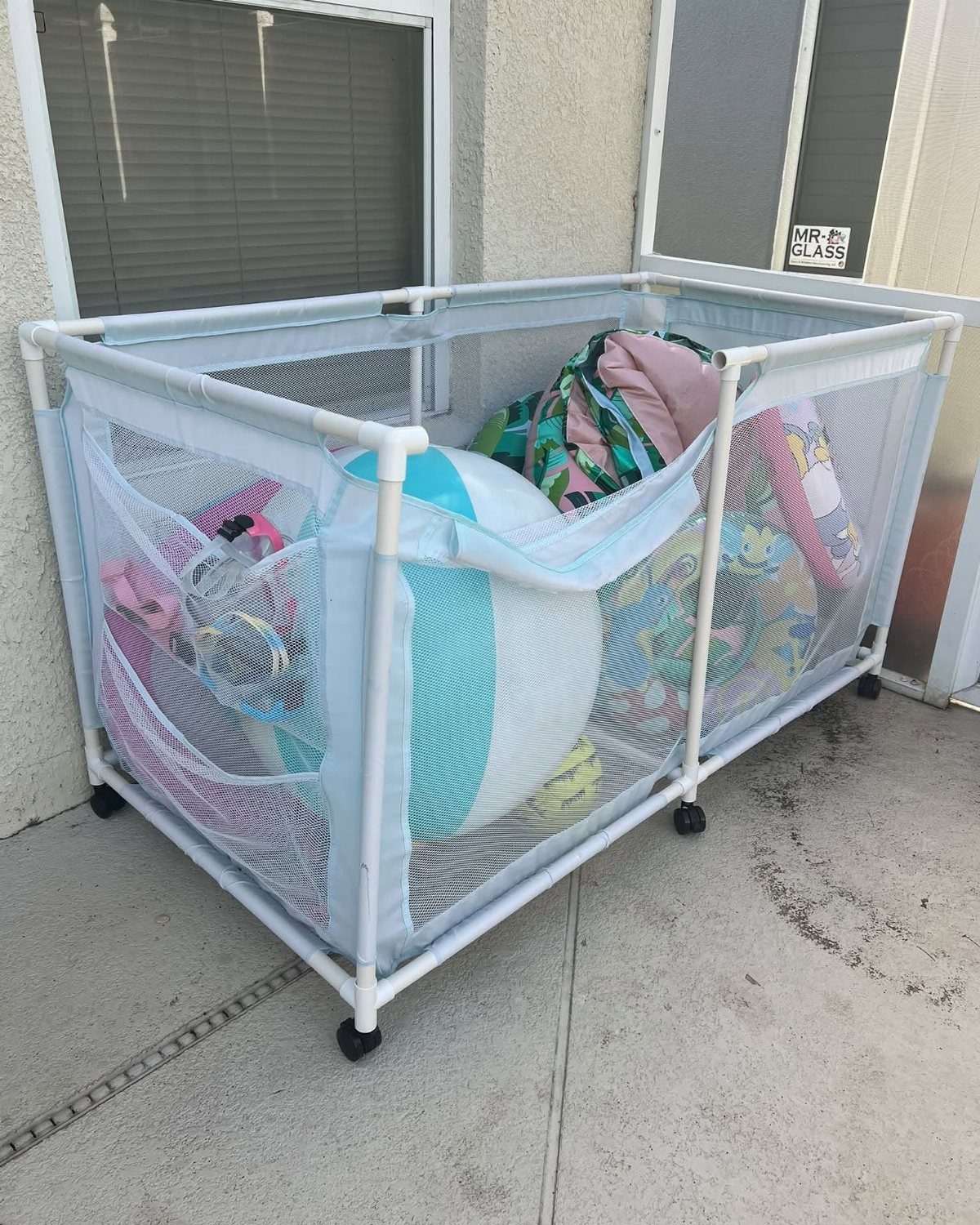 A white PVC frame with blue mesh sides containing various colorful inflatable pool toys.