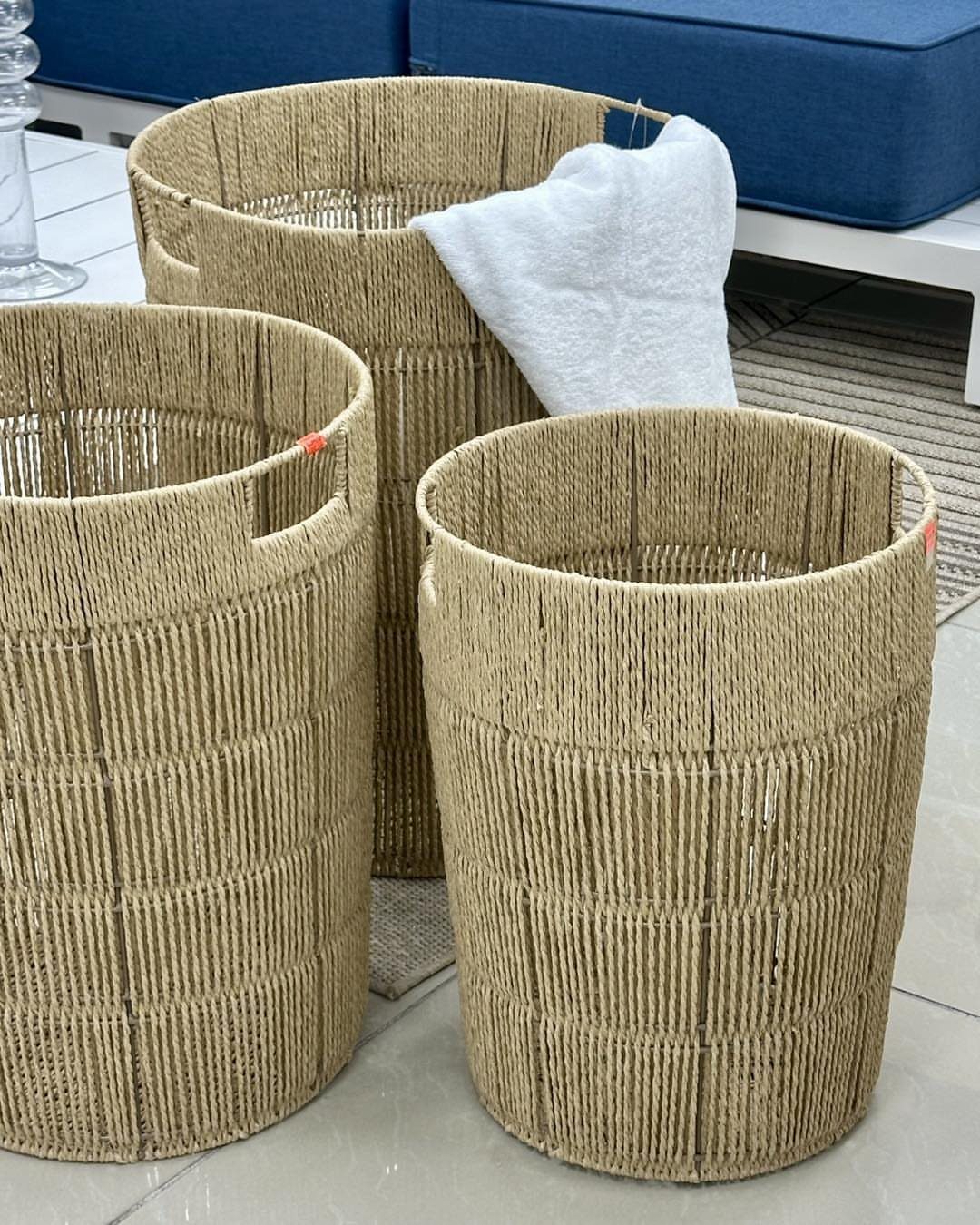 Three tall woven jute baskets sitting on a floor near blue outdoor furniture.