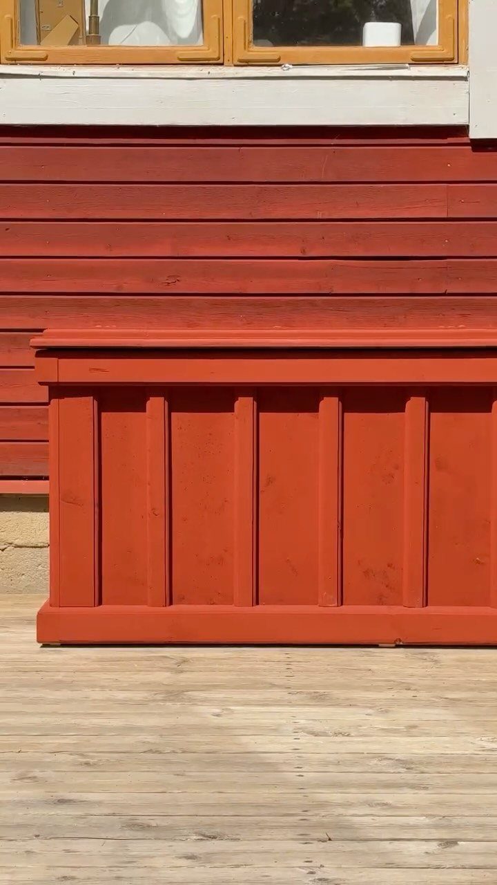 A large red wooden storage box sitting on a light wooden deck against a red wall.