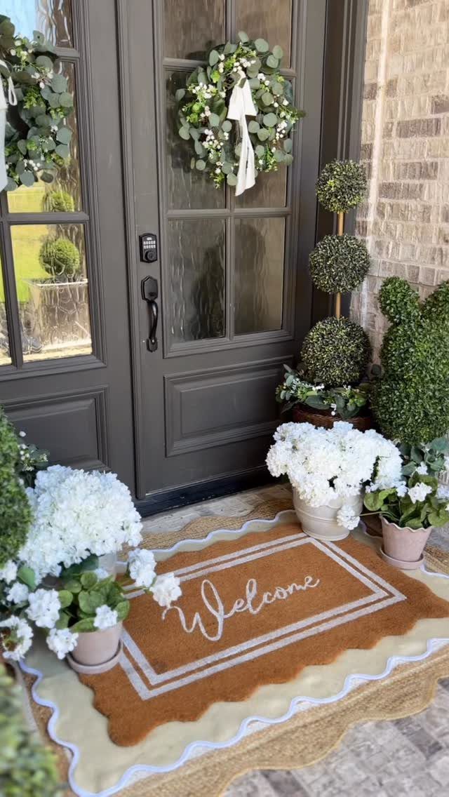 A brown welcome mat layered over a cream scalloped rug in front of a dark grey door.