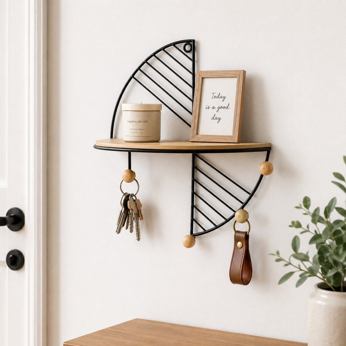 A wooden wall shelf with black wire accents holding a candle, a framed sign, and hanging keys.