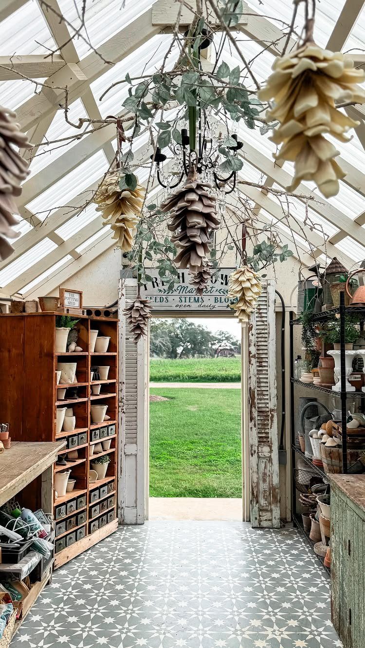 Interior of a bright greenhouse with white wooden beams, patterned tiles, and wooden shelves filled with pots.
