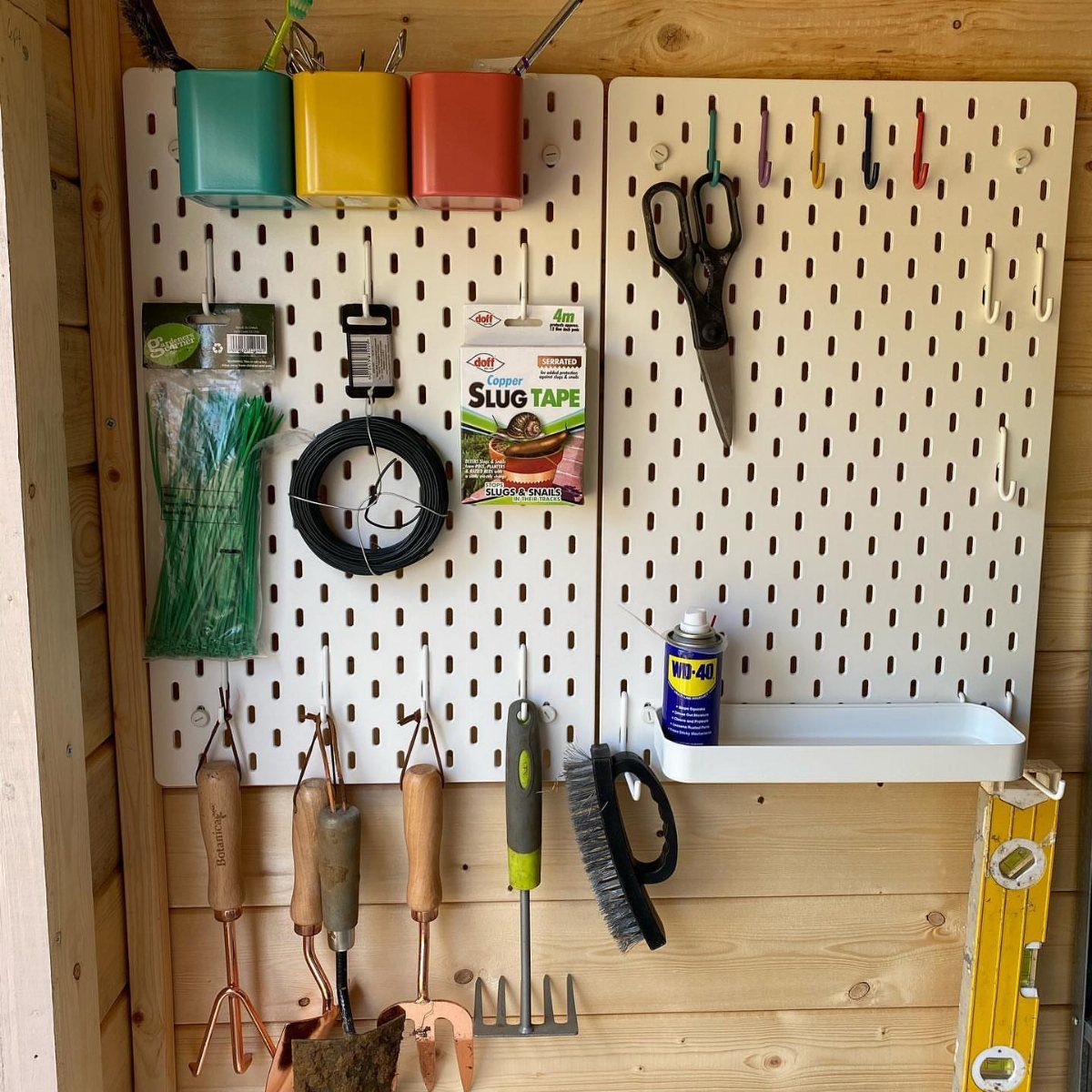 White pegboards mounted on a wooden wall holding various gardening tools and colorful containers.