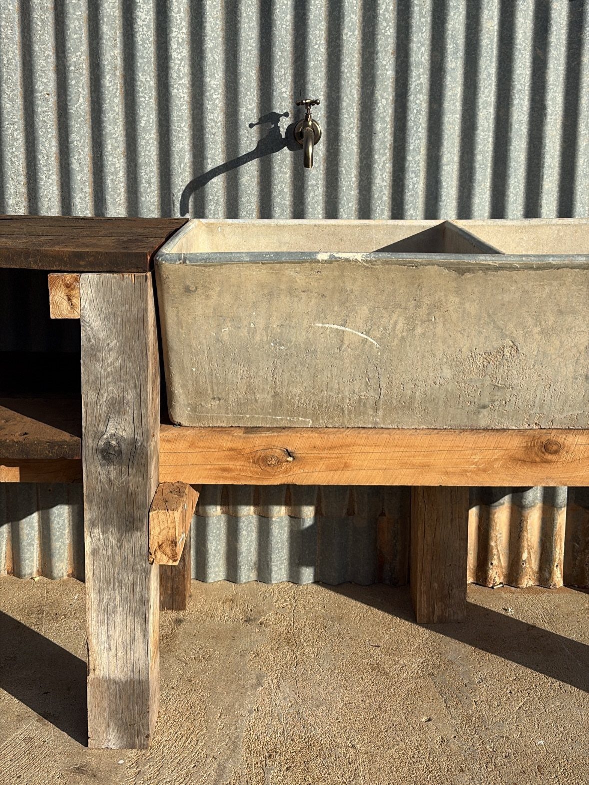 A concrete sink mounted on a wooden bench against a corrugated metal wall.