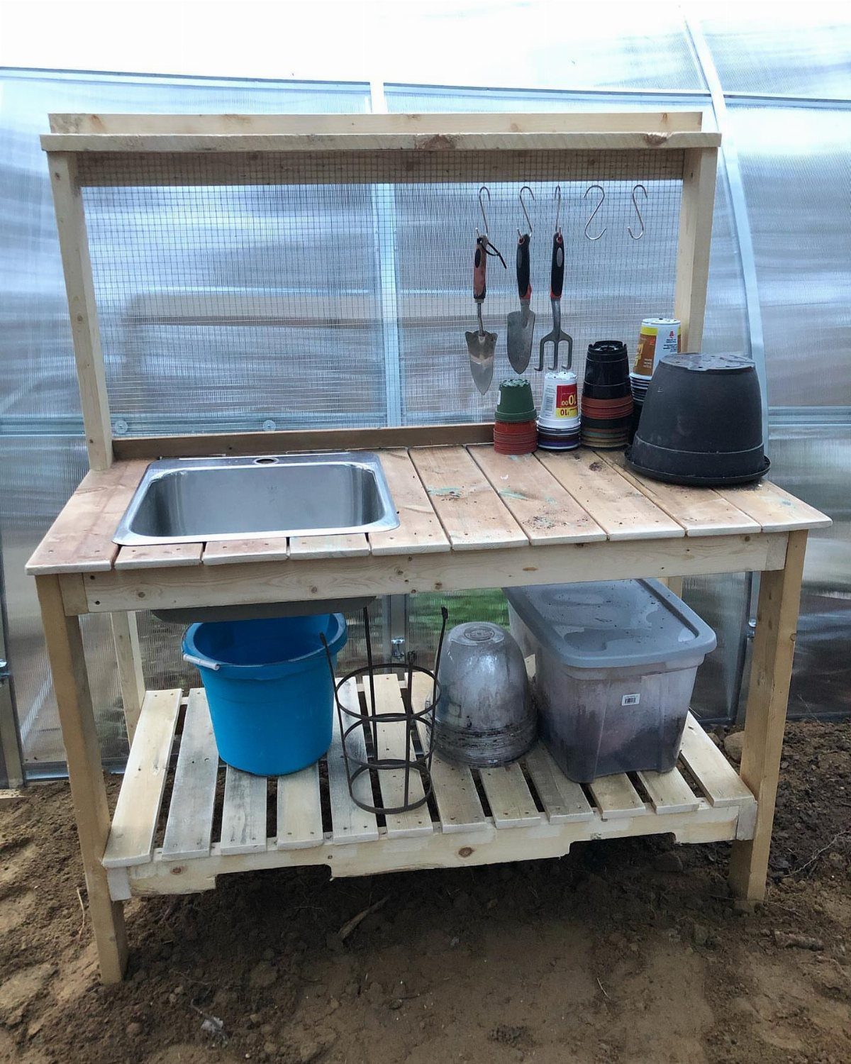 A wooden potting bench with a built-in stainless steel sink and gardening tools hanging above.